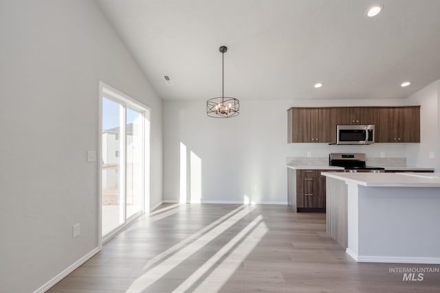 kitchen featuring appliances with stainless steel finishes, decorative light fixtures, light wood-type flooring, a chandelier, and lofted ceiling