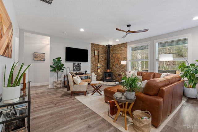 living room featuring ceiling fan, a wood stove, and light wood-type flooring