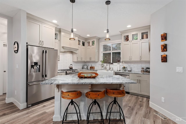 kitchen featuring hanging light fixtures, light stone countertops, light wood-type flooring, stainless steel appliances, and a center island