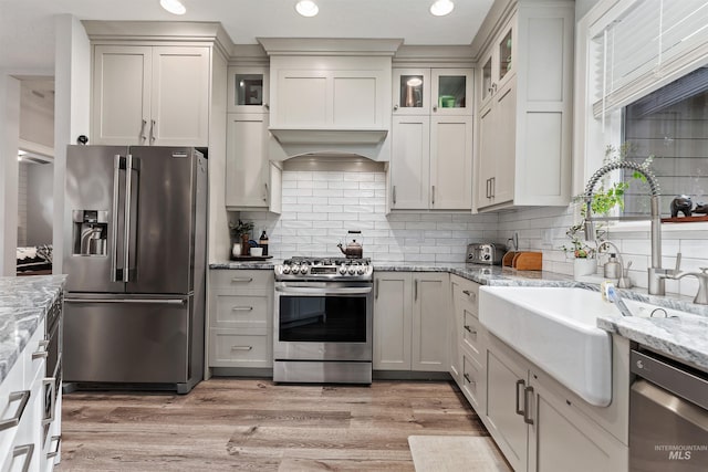 kitchen with sink, light wood-type flooring, stainless steel appliances, light stone counters, and decorative backsplash