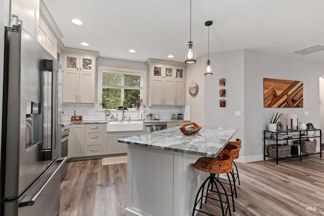 kitchen featuring hardwood / wood-style floors, light stone counters, appliances with stainless steel finishes, sink, and a center island