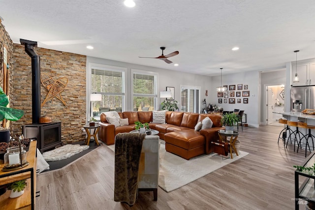 living room featuring light hardwood / wood-style flooring, a textured ceiling, a wood stove, and ceiling fan