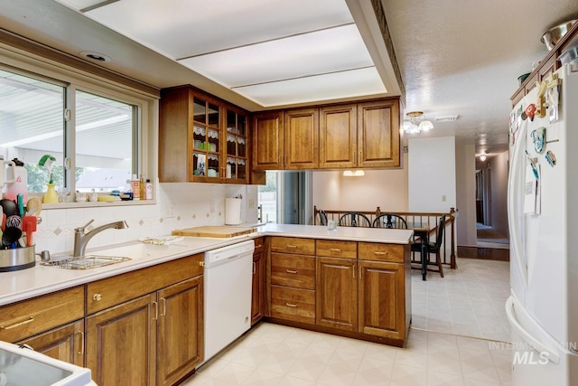 11360 W Lake Hazel Rd, Boise, ID 83709 - kitchen with white appliances, brown cabinets, a peninsula, light countertops, and glass insert cabinets
