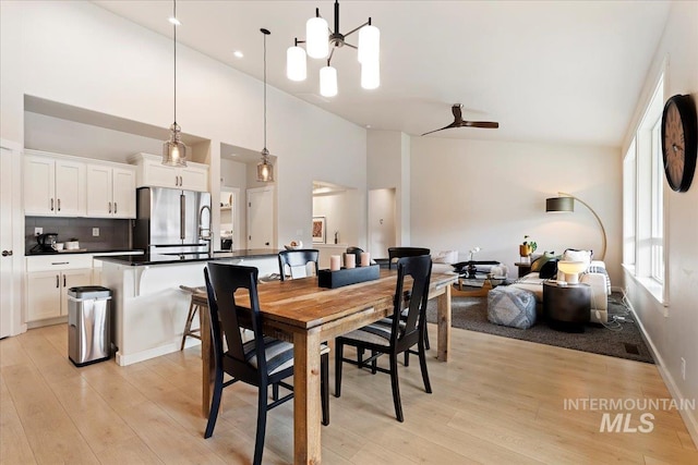 dining space featuring ceiling fan with notable chandelier, a high ceiling, light wood-type flooring, and baseboards