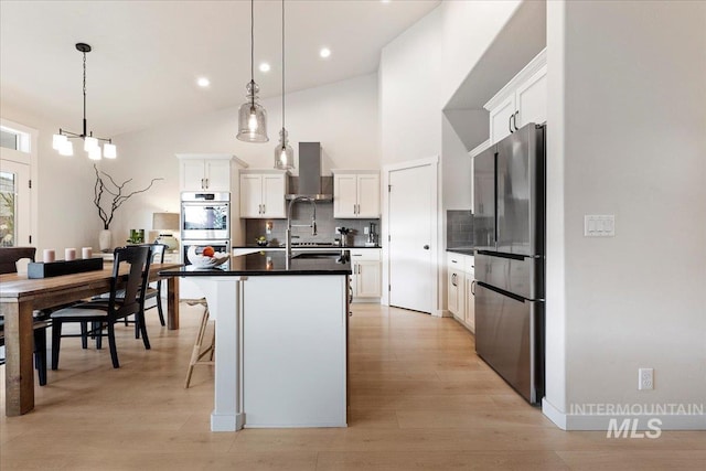 kitchen with decorative backsplash, dark countertops, appliances with stainless steel finishes, a kitchen island with sink, and wall chimney range hood