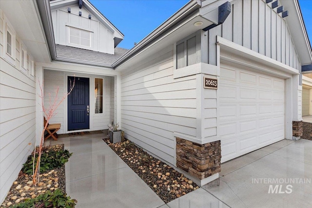 doorway to property featuring a garage, stone siding, board and batten siding, and driveway