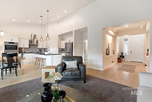 living room with light wood-style flooring, a high ceiling, baseboards, and recessed lighting