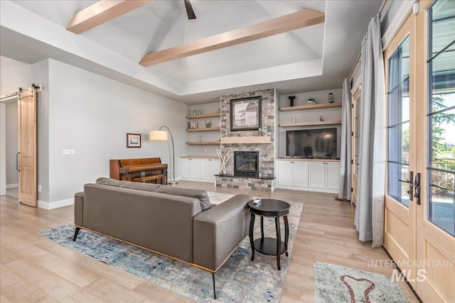 living room featuring built in shelves, a raised ceiling, a barn door, light hardwood / wood-style flooring, and a fireplace