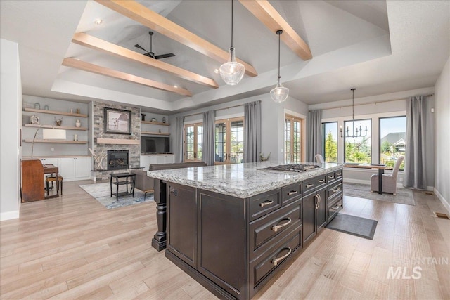 kitchen with light stone counters, ceiling fan, a stone fireplace, hanging light fixtures, and an island with sink