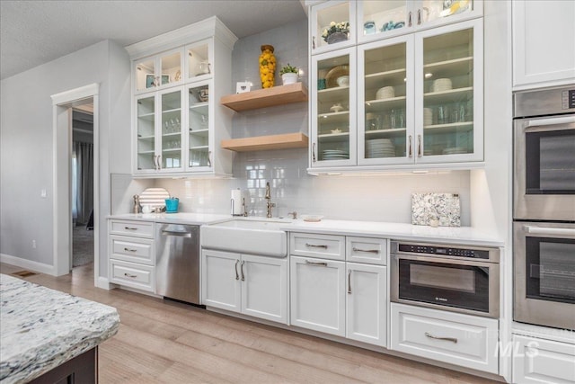 kitchen featuring light wood-type flooring, backsplash, stainless steel appliances, sink, and white cabinets