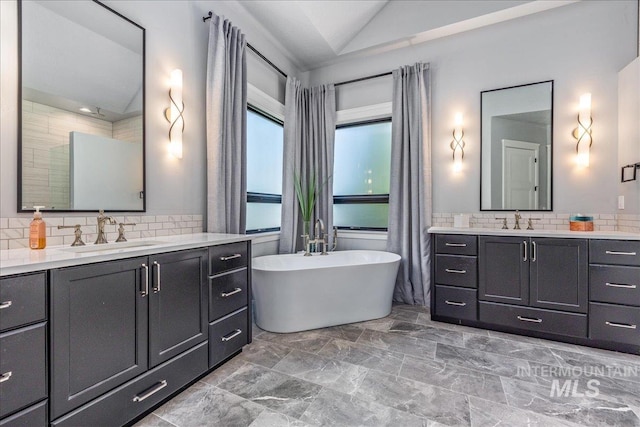 bathroom with decorative backsplash, a bathtub, vanity, and vaulted ceiling