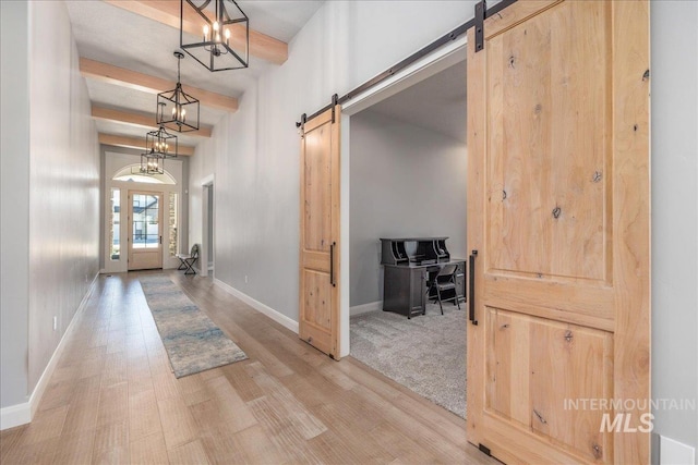 hall with beamed ceiling, a barn door, light hardwood / wood-style floors, and a notable chandelier