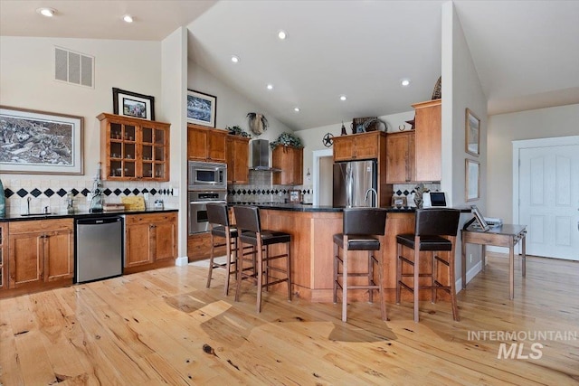 kitchen with dark countertops, visible vents, appliances with stainless steel finishes, a peninsula, and wall chimney exhaust hood