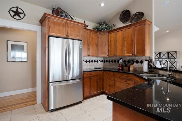 kitchen with freestanding refrigerator, vaulted ceiling, brown cabinets, and a sink