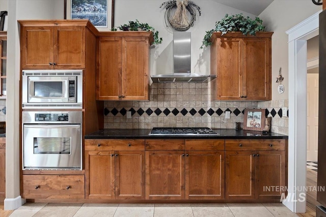 kitchen featuring wall chimney exhaust hood, appliances with stainless steel finishes, dark countertops, and brown cabinets