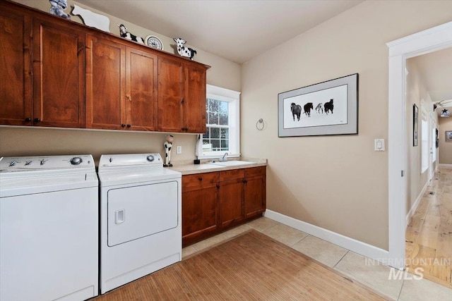 laundry room with cabinet space, light tile patterned floors, baseboards, independent washer and dryer, and a sink