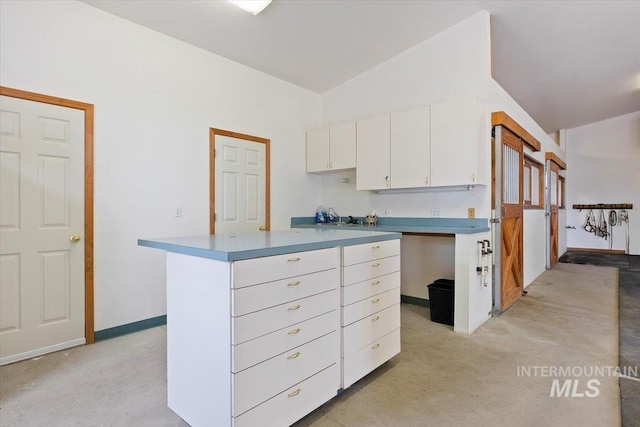 kitchen with a kitchen island, white cabinetry, vaulted ceiling, and baseboards