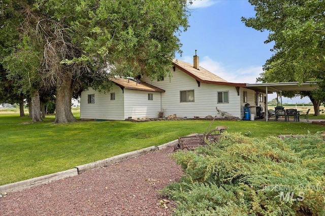 back of property with a yard, an attached carport, and a chimney