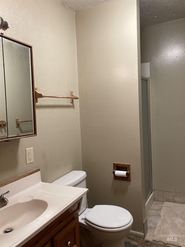 bathroom with a textured wall, a shower stall, toilet, and vanity