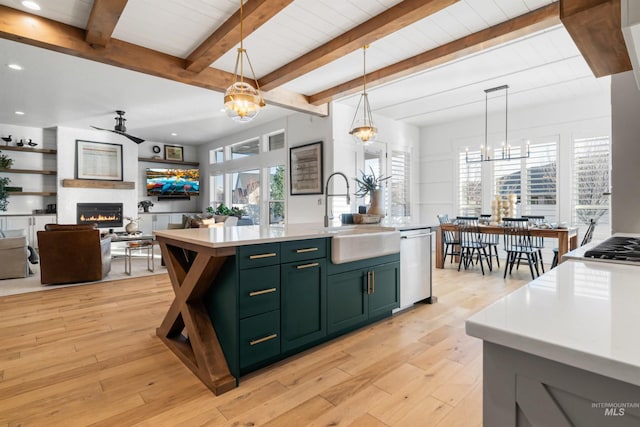 kitchen with a sink, a large fireplace, green cabinets, light countertops, and dishwasher