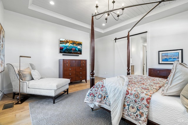 bedroom with a barn door, wood finished floors, crown molding, and a raised ceiling