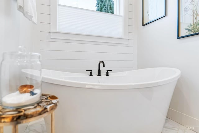 full bathroom with marble finish floor and a freestanding bath