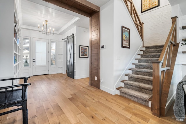 entryway with stairway, light wood-style flooring, ornamental molding, a barn door, and a chandelier