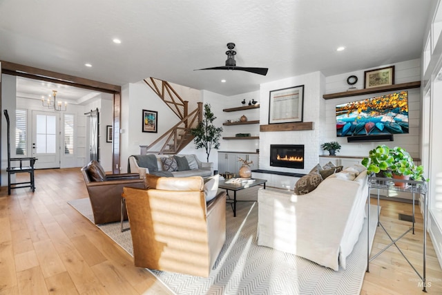 living area with recessed lighting, light wood-style flooring, ceiling fan with notable chandelier, and a large fireplace