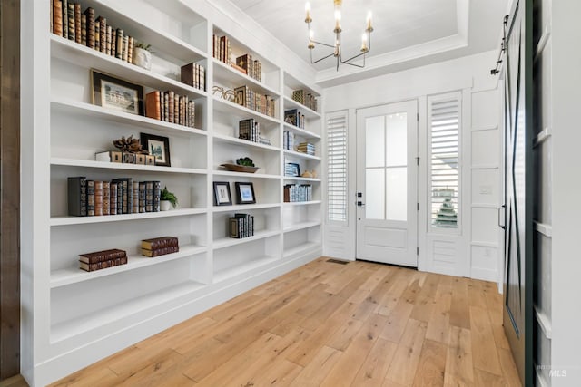 entrance foyer featuring light wood-type flooring, a barn door, ornamental molding, a notable chandelier, and a raised ceiling