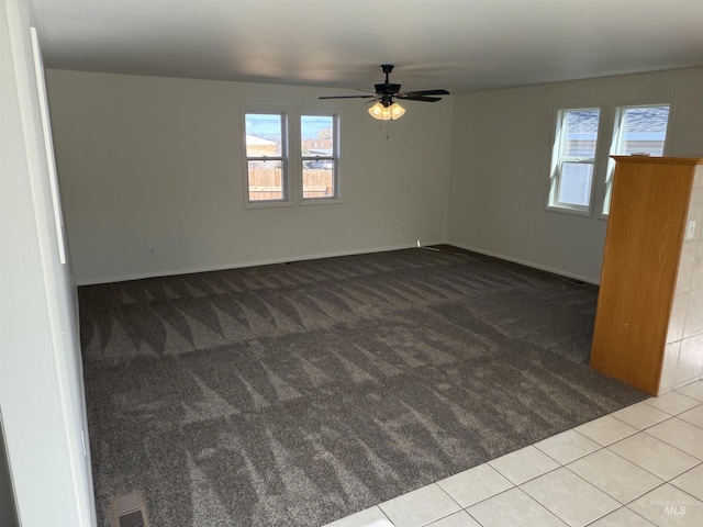 carpeted spare room with tile patterned flooring, visible vents, ceiling fan, and a healthy amount of sunlight