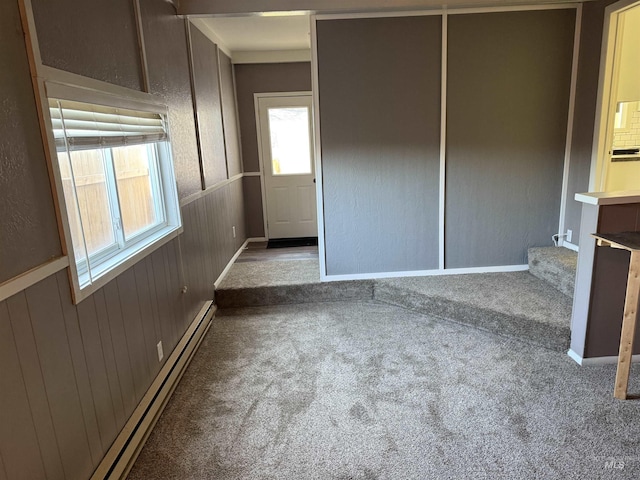 unfurnished room with a baseboard radiator, wooden walls, a textured wall, and carpet
