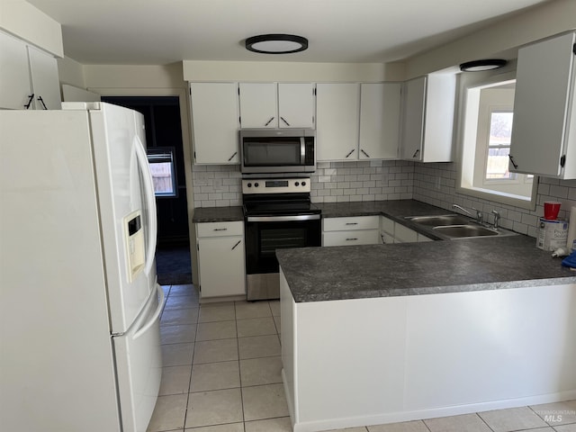 kitchen featuring a peninsula, stainless steel appliances, dark countertops, a sink, and backsplash