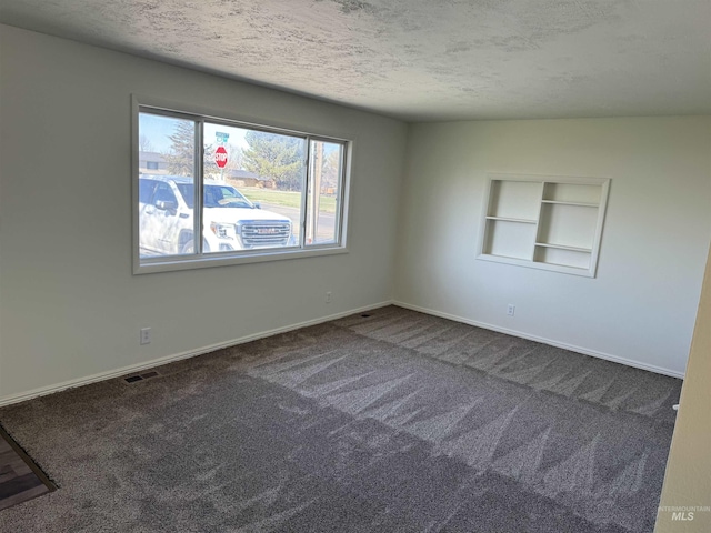 carpeted empty room with a textured ceiling, baseboards, built in shelves, and visible vents