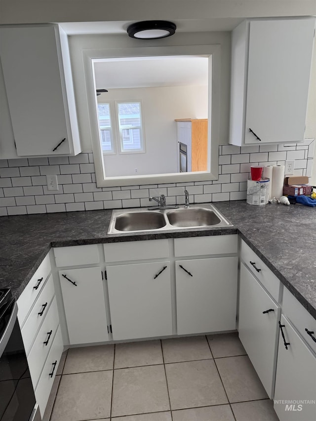 kitchen featuring dark countertops, tasteful backsplash, white cabinetry, a sink, and light tile patterned floors