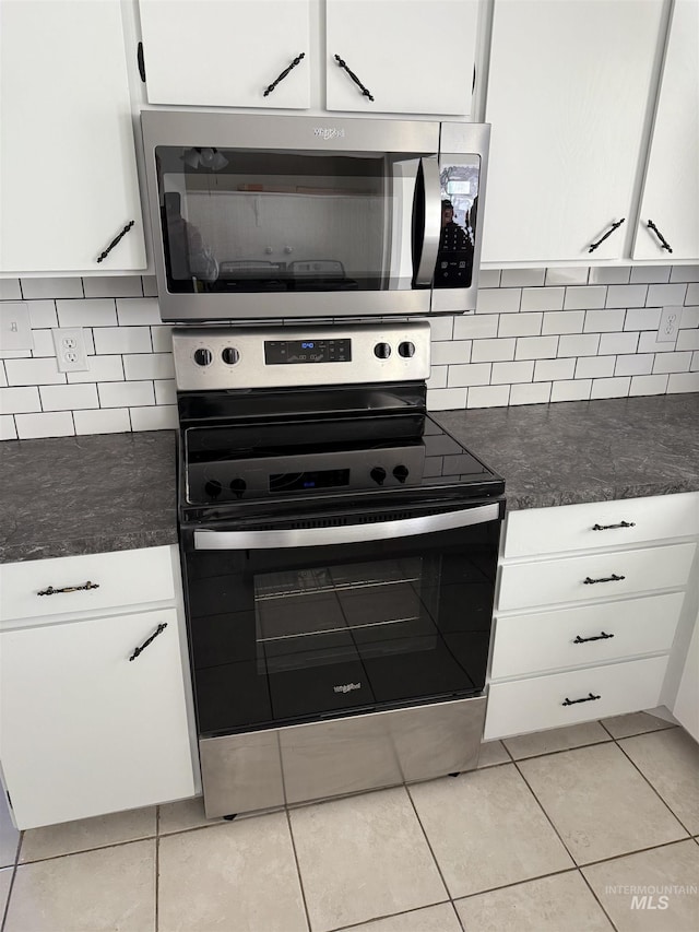 kitchen with stainless steel appliances, light tile patterned floors, dark countertops, white cabinets, and decorative backsplash