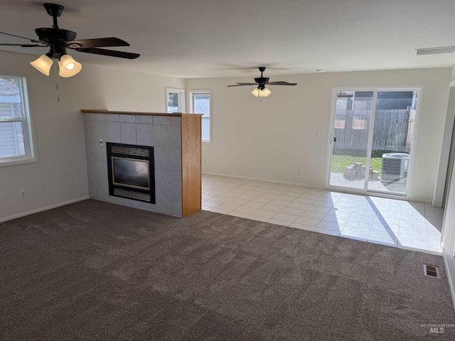 unfurnished living room featuring light tile patterned flooring, light colored carpet, a tiled fireplace, and a ceiling fan