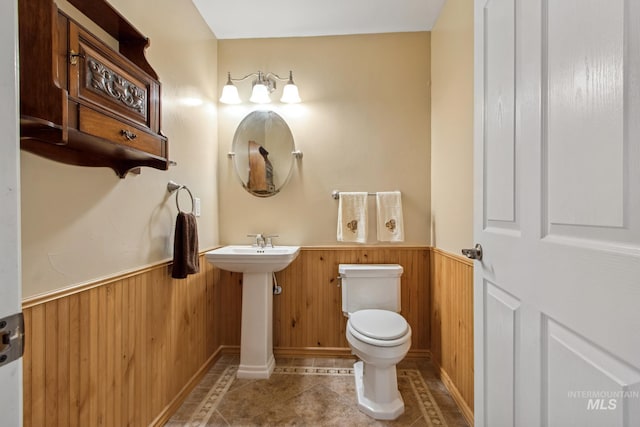 half bath featuring wainscoting, wood walls, and toilet