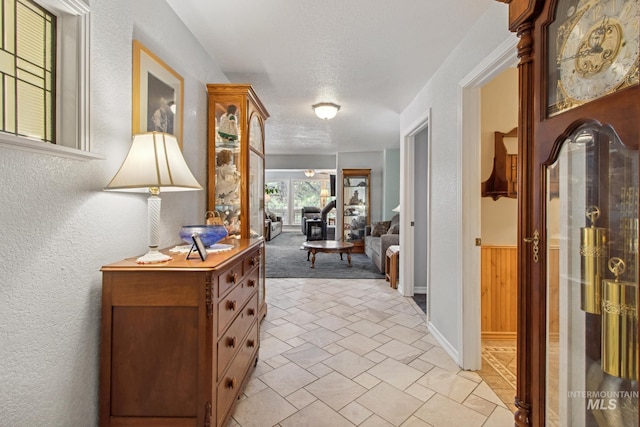 hallway featuring a textured ceiling, a textured wall, and a wainscoted wall