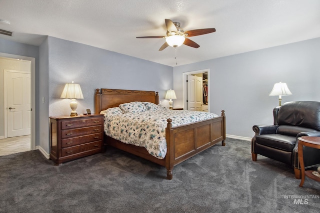 bedroom featuring ceiling fan, a spacious closet, baseboards, and dark colored carpet