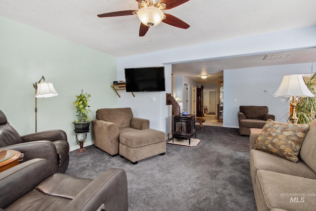 carpeted living room with a wood stove, a textured ceiling, visible vents, and a ceiling fan