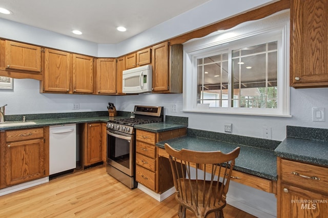 kitchen featuring a sink, white appliances, brown cabinets, and light wood-style floors