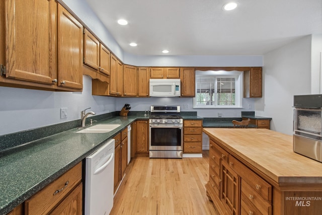 kitchen with white appliances, butcher block countertops, brown cabinetry, and a sink