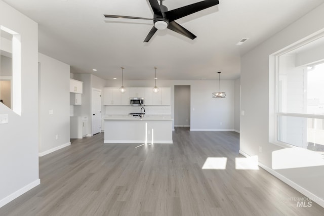 unfurnished living room with recessed lighting, baseboards, ceiling fan, a sink, and light wood-type flooring