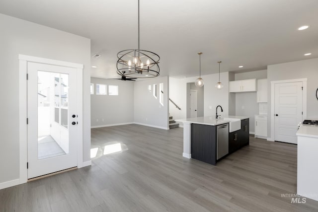 kitchen with a sink, pendant lighting, stainless steel dishwasher, light countertops, and a chandelier