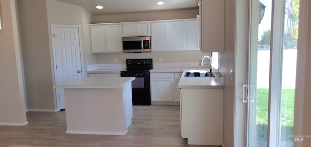 kitchen with white cabinets, black electric range oven, light hardwood / wood-style floors, sink, and a center island