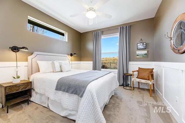 bedroom with a wainscoted wall, light carpet, and ceiling fan