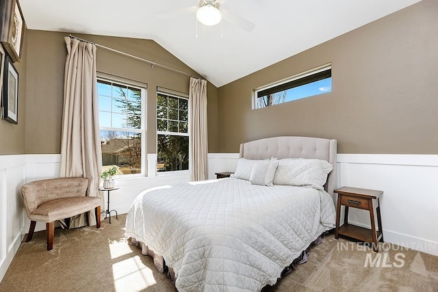 carpeted bedroom with wainscoting, ceiling fan, and vaulted ceiling