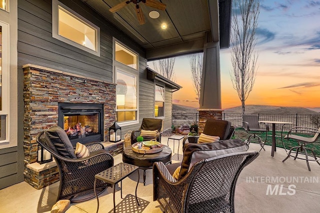 patio terrace at dusk with a ceiling fan and an outdoor living space with a fireplace