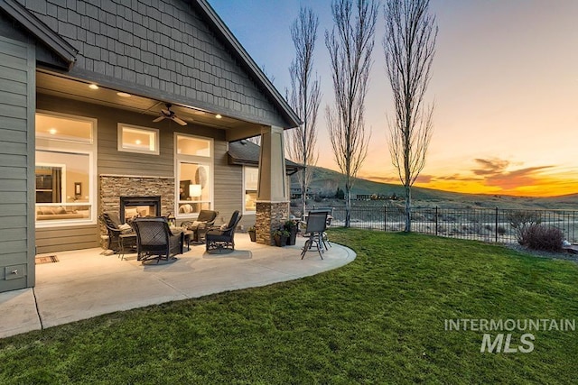 yard at dusk featuring an outdoor living space with a fireplace, a patio, ceiling fan, and fence