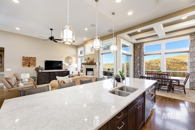 kitchen featuring light stone countertops, dark wood finished floors, a stone fireplace, coffered ceiling, and a sink